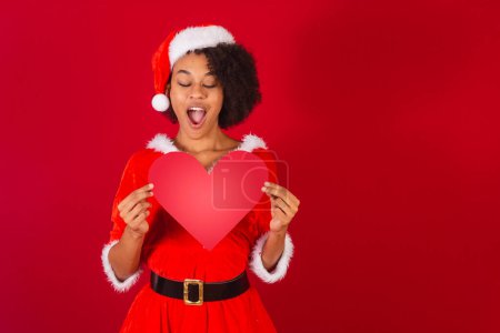 Téléchargez les photos : Belle femme brésilienne noire, habillée en Père Noël claus, maman claus, tenant coeur rouge - en image libre de droit