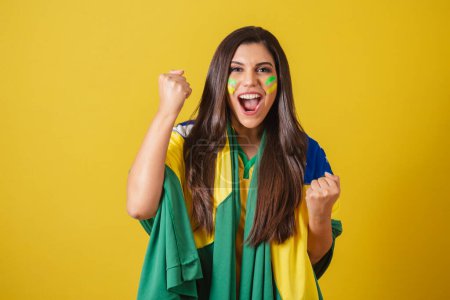 Téléchargez les photos : Femme supporter du Brésil, coupe du monde 2022, championnat de football, en utilisant le drapeau comme cape, objectif criant ! Faire la fête et célébrer le jeu Brésil. - en image libre de droit