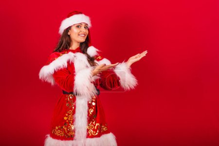 Foto de Mujer brasileña vestida con ropa de Navidad, Santa Claus. mostrando algo a la derecha. - Imagen libre de derechos