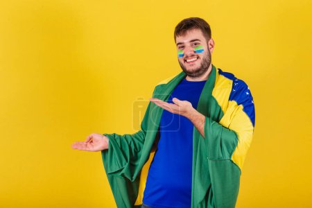 Photo for Brazilian caucasian man, soccer fan from brazil, pointing hands some product to left, photo for ad. indicating. - Royalty Free Image