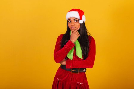 Photo for Beautiful black Brazilian woman, dressed in Christmas clothes, Santa Claus, thinking. - Royalty Free Image