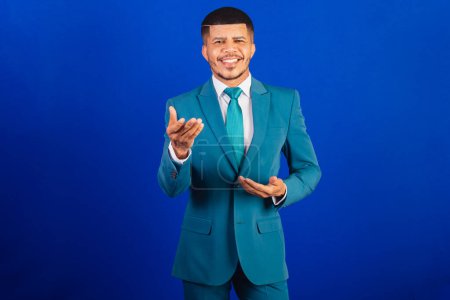 Foto de Hombre negro brasileño, vestido con traje y corbata azul. hombre de negocios. presentando algo, apuntando a la cámara - Imagen libre de derechos
