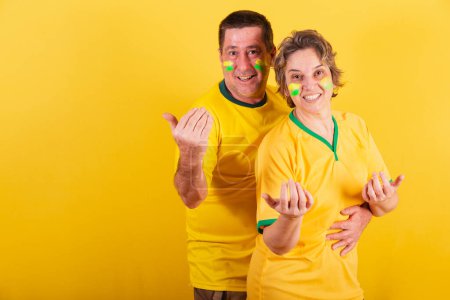 Foto de Pareja adulta, fanáticos del fútbol brasileño aislados en amarillo - Imagen libre de derechos