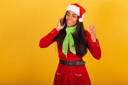 Foto de Hermosa mujer brasileña negra vestida con ropa de navidad, santa claus, teléfono inteligente y llamada de voz - Imagen libre de derechos