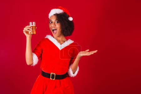 Téléchargez les photos : Belle femme brésilienne noire, habillée en Père Noël, maman Claude, tenant un verre de bière - en image libre de droit