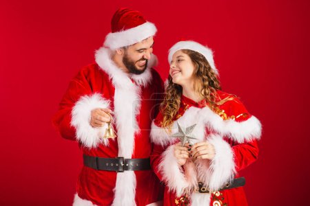 Téléchargez les photos : Couple brésilien, habillé en vêtements de Noël, Père Noël, tenant des décorations de Noël, étoile, cloche. - en image libre de droit