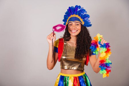 Téléchargez les photos : Belle femme brésilienne noire, avec des vêtements frevo, carnaval. en coiffe de plumes de carnaval. avec masque de carnaval et collier dans les mains. - en image libre de droit