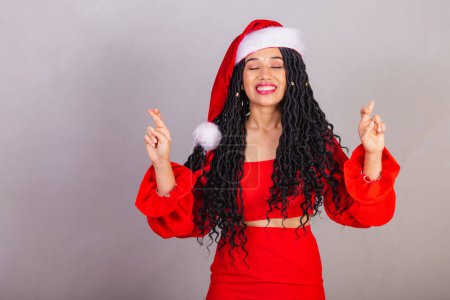 Photo for Brazilian black woman wearing christmas clothes, merry christmas, smiling, fingers crossed cheering, wishing, sign of luck. - Royalty Free Image