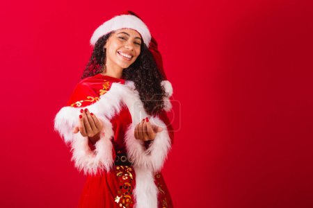 Photo for Beautiful brazilian black woman, dressed as santa claus, christmas clothes. welcome, inviting with hands. - Royalty Free Image