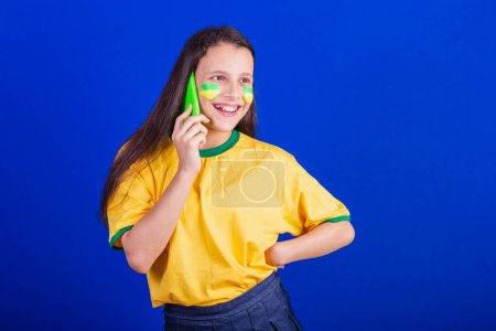 Photo for Young girl, soccer fan from Brazil. holding cellphone, voice call. Smartphone. applications. - Royalty Free Image
