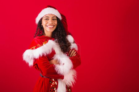 Téléchargez les photos : Belle femme noire brésilienne, habillée en Père Noël claus, vêtements de Noël. sourire les bras croisés. - en image libre de droit