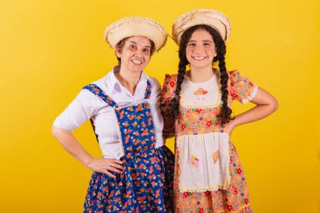 Foto de Abuela y nieta vestidas con ropa típica de Festa Junina. Manos en las caderas, sonriendo. - Imagen libre de derechos