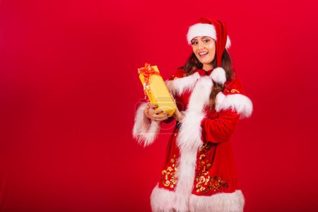Photo for Brazilian woman dressed in Christmas clothes, Santa Claus. showing a yellow gift. - Royalty Free Image