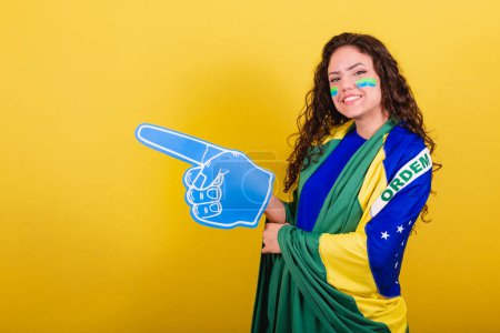 Foto de Mujer fanática del fútbol, fan de Brasil, copa del mundo, con guante de espuma. apuntando al espacio negativo, anuncio, texto o publicidad. Lado izquierdo. - Imagen libre de derechos