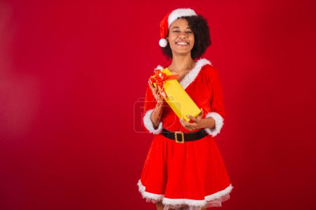 Photo for Beautiful black brazilian woman, dressed as santa claus, mama claus, happy holding present - Royalty Free Image