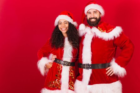 Photo for Brazilian couple, dressed for christmas, santa claus, mummy claus. black woman and caucasian man. Smiling at camera. - Royalty Free Image