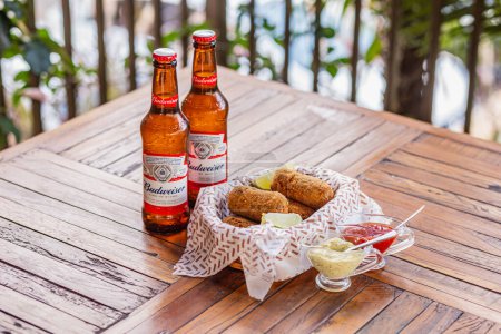 Photo for Chicken croquette, typical Brazilian snack, served with lemon slices, chili sauce and mayonnaise On the wooden table served with the famous budeveiser beer. - Royalty Free Image
