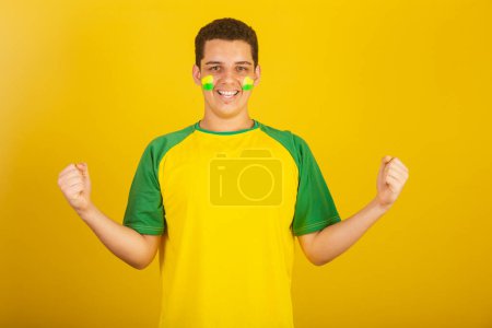 Téléchargez les photos : Jeune Brésilien fan de foot. habillé en vert, et jaune, célébrant. - en image libre de droit
