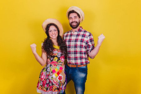 Photo for Beautiful couple dressed in typical clothes for a Festa Junina. Arraia de Sao Joao. Celebrating, victory, cheering. - Royalty Free Image