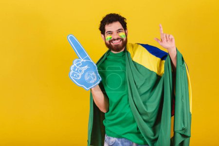 Foto de Hombre, brasileño, barbudo, fanático del fútbol de Brasil, usando el dedo de espuma haciendo coreografía de baile para la victoria del equipo, gol. - Imagen libre de derechos