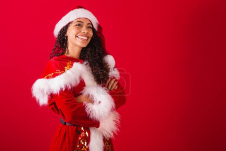 Foto de Hermosa mujer negra brasileña, vestida como santa claus, ropa de Navidad. sonriendo con los brazos cruzados. - Imagen libre de derechos