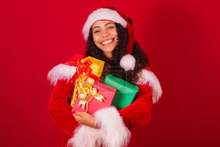 Photo for Beautiful brazilian black woman, dressed as santa claus, christmas clothes. holding three gifts. - Royalty Free Image