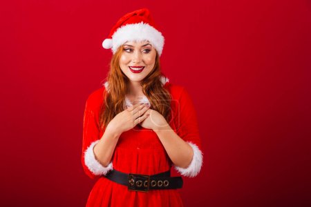 Photo for Beautiful Brazilian red-haired woman, dressed in Christmas clothes, Santa Claus. hands on chest, gratitude. - Royalty Free Image