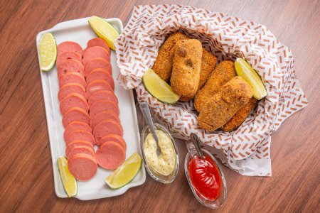 Photo for Chicken croquette and Cambu sausage,typical Brazilian snack, served with lemon slices, chili sauce and mayonnaise. on wooden table - Royalty Free Image