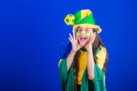 Téléchargez les photos : Jeune fille, fan de football du Brésil. habillé en chapeau et drapeau. hurlant objectif. - en image libre de droit