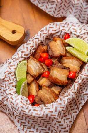 Photo for Crackling, fried pork, bacon, typical Brazilian food, served with lemon slices. peppers - Royalty Free Image