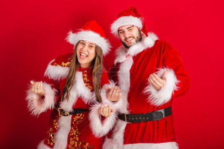 Foto de Pareja brasileña con ropa de Navidad, Santa Claus. llamando con las manos, invitando. - Imagen libre de derechos