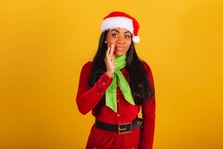 Téléchargez les photos : Belle femme brésilienne noire, vêtue de vêtements de Noël, Père Noël claus, révélant le secret. - en image libre de droit