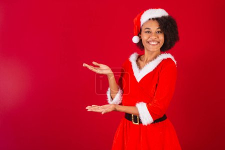 Photo for Beautiful black brazilian woman, dressed as santa claus, mama claus, presenting product or information on the side - Royalty Free Image