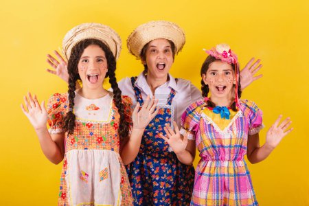 Photo for Grandmother and her two granddaughters dressed in typical Festa Junina clothes. Surprised, amazed, wow, incredible. - Royalty Free Image