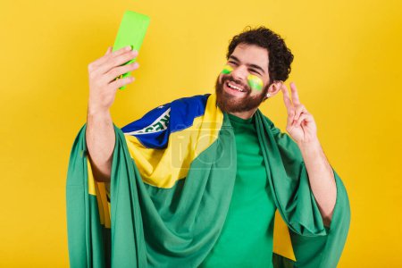 Foto de Hombre caucásico con barba, brasileño, fanático del fútbol de Brasil, tomando autorretrato con teléfono celular, selfie, teléfono inteligente. - Imagen libre de derechos