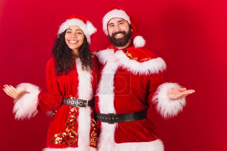 Photo for Brazilian couple, dressed for christmas, santa claus, mummy claus. welcome, inviting, black woman and caucasian man. - Royalty Free Image