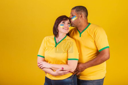 Téléchargez les photos : Couple, femme rousse et homme noir, fans de football brésilien. Bras croisés, souriant à la caméra. - en image libre de droit