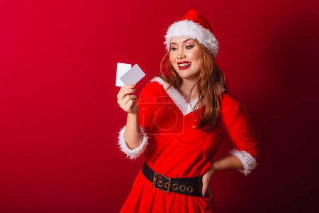 Photo for Beautiful Brazilian red-haired woman, dressed in Christmas clothes, Santa Claus. holding credit cards. - Royalty Free Image
