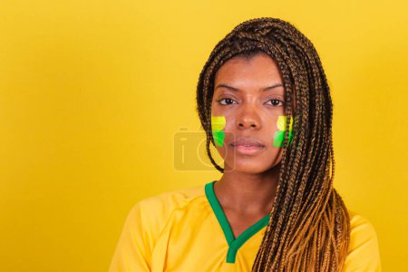 Foto de Mujer negra joven aficionada al fútbol brasileño. foto de cerca, mirando a la cámara seria. - Imagen libre de derechos