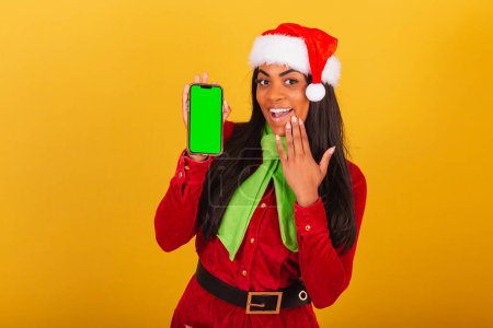Photo for Beautiful black Brazilian woman, dressed in christmas clothes, santa claus, smartphone and showing green chroma screen. - Royalty Free Image