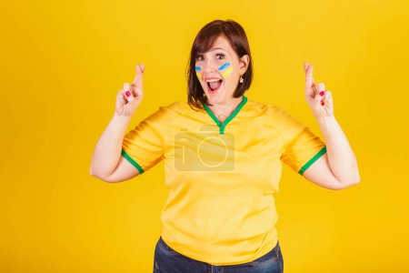 Foto de Mujer pelirroja, fan del fútbol brasileño. señal de la suerte, los dedos cruzados, deseando, animando. - Imagen libre de derechos