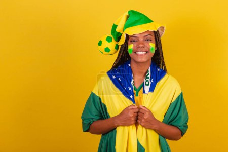 Téléchargez les photos : Femme noire jeune fan de football brésilien. portant chapeau et drapeau. Habillé pour le jeu. - en image libre de droit