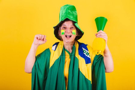 Photo for Adult adult woman, soccer fan from brazil, wearing flag and hat, using horn noise, cheering. - Royalty Free Image