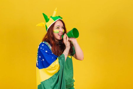 Foto de Caucásico pelirroja mujer brasileña fútbol fan gritando promoción usando mega teléfono, publicidad foto. - Imagen libre de derechos