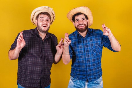 Photo for Two friends wearing typical clothes for the Festa Junina. Fingers crossed, twisting, wishing. Luck - Royalty Free Image