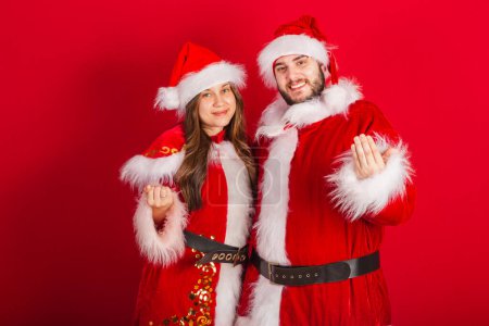 Téléchargez les photos : Couple brésilien avec vêtements de Noël, Père Noël claus. appeler avec les mains, inviter. - en image libre de droit
