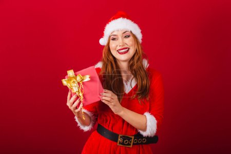 Photo for Beautiful Brazilian red-haired woman, dressed in Christmas clothes, Santa Claus. holding red gift. - Royalty Free Image