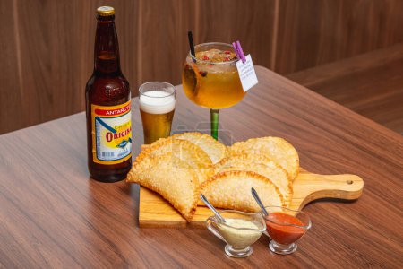 Photo for Fried pastry, fogazza, meat pastry, cheese pastry, served with mayonnaise and chili sauce, timico Brazilian bar snack. Served gin and tonic drink. Original famous beer. - Royalty Free Image