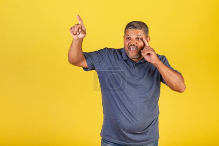 Foto de Hombre negro brasileño, adulto señalando algo distante con su dedo, sorprendido. - Imagen libre de derechos