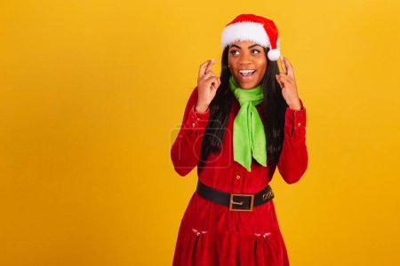 Photo for Beautiful black Brazilian woman, dressed in christmas clothes, santa claus, cheering, fingers crossed, lucky. - Royalty Free Image